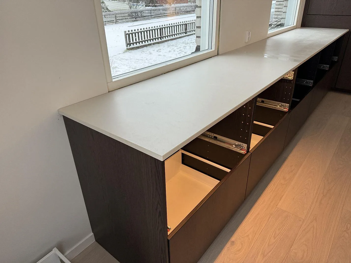 Lång bänkskiva i matt Dekton Aeris vid stora fönster och mörka köksstommar i Mariestad.