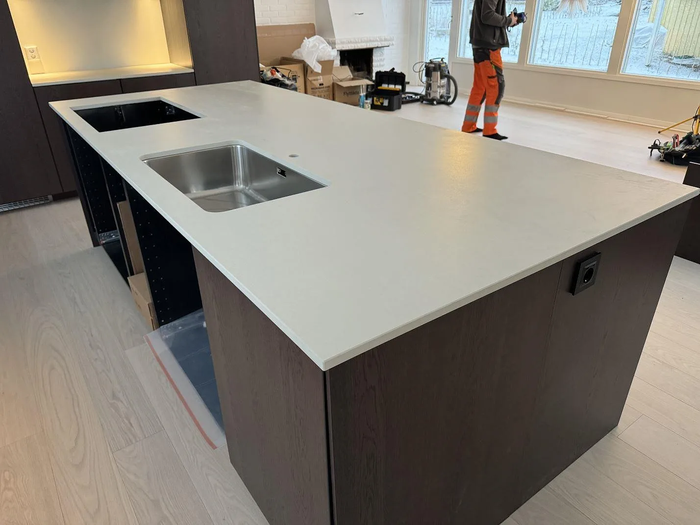Stor köksö i matt Dekton Aeris med rostfri diskho och öppning för häll under montering i Mariestad.