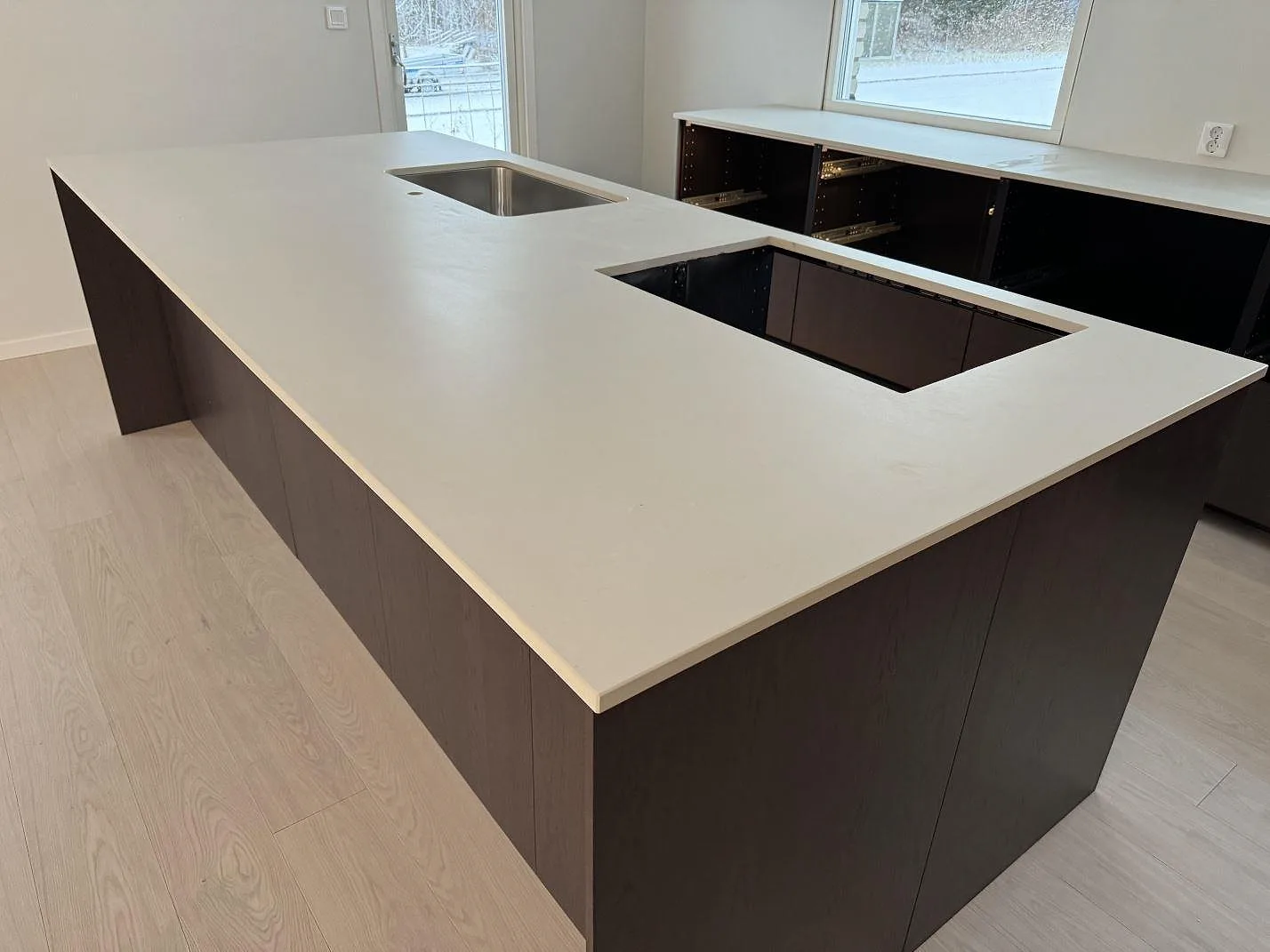 Närbild på matt Dekton Aeris som köksö med underlimmad diskho, hällurtag och bänk vid fönster i Mariestad.