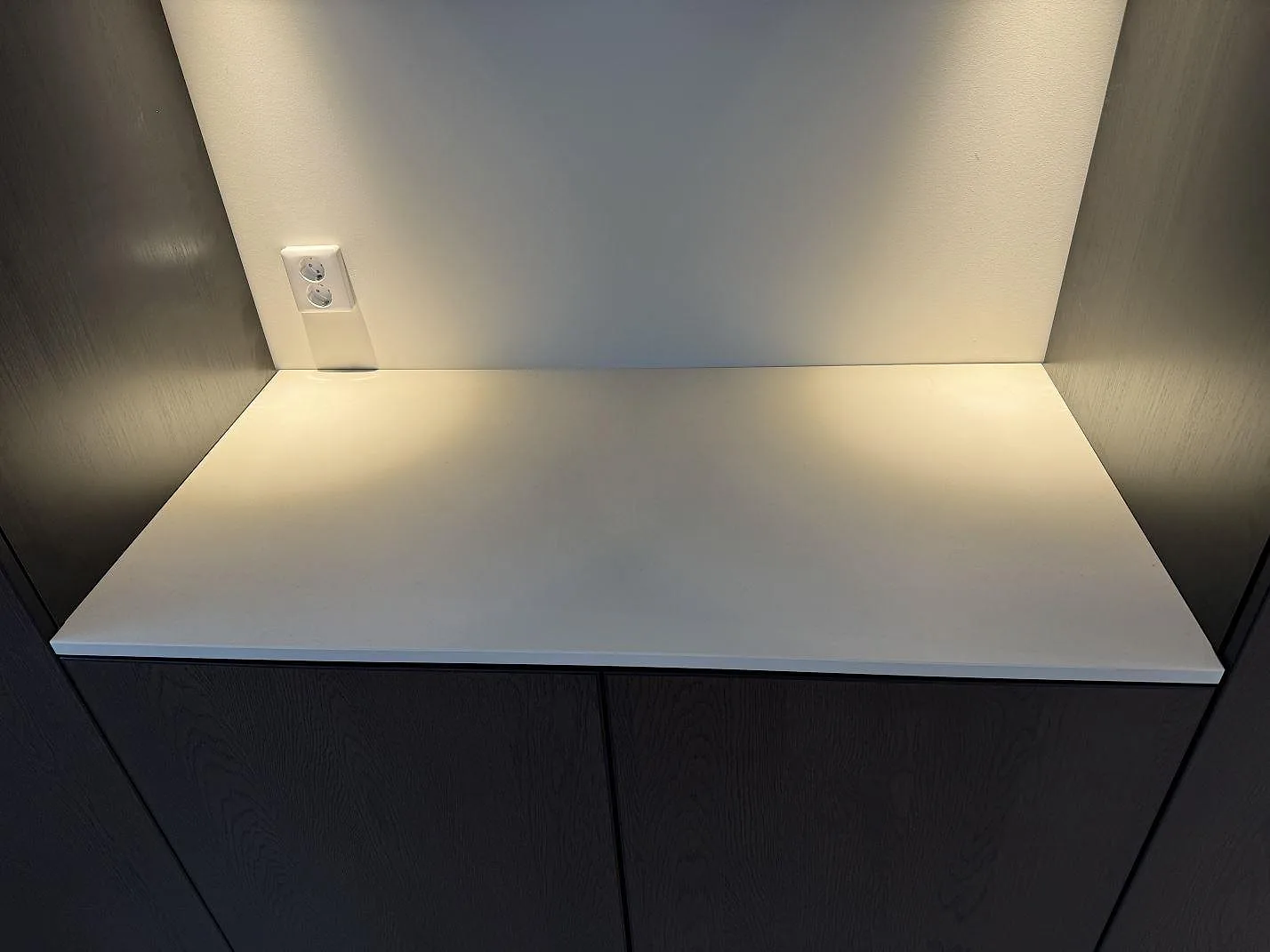 Rak detaljbild av matt Dekton Aeris som bänkskiva mellan mörka skåp och belyst vägg i Mariestad.