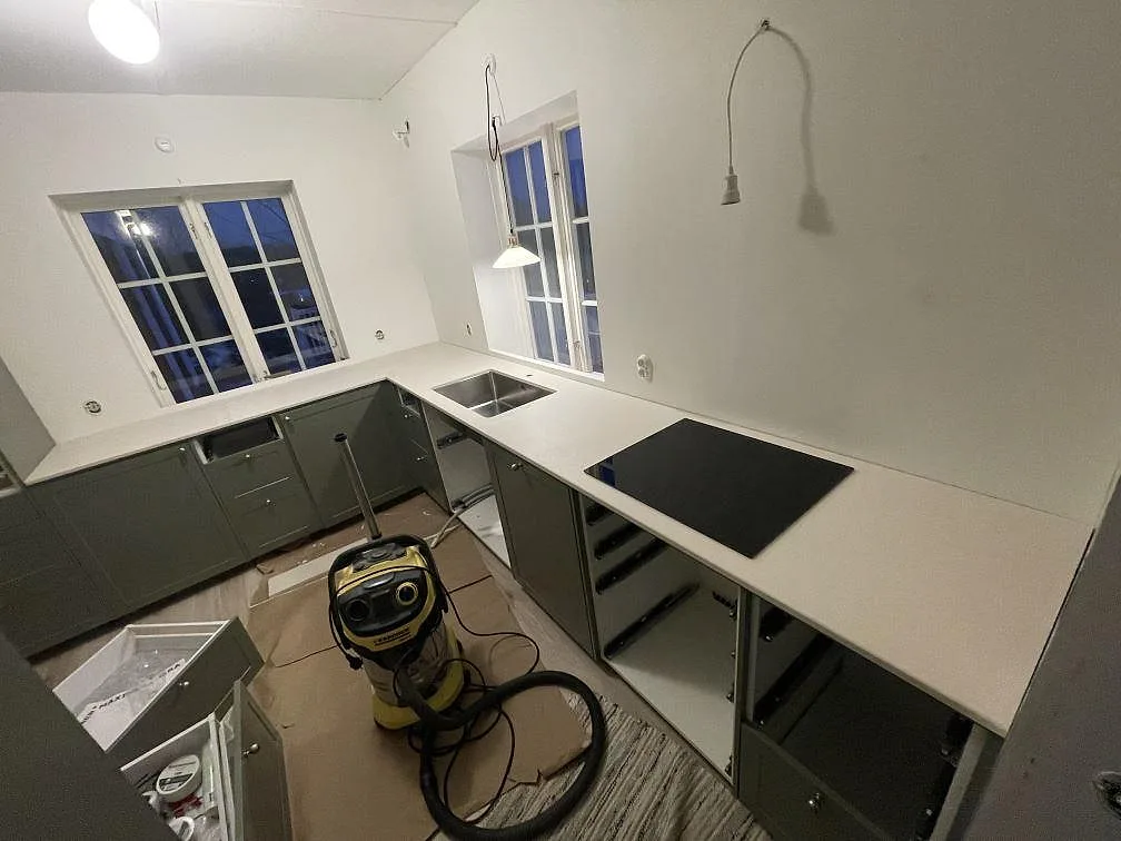 Köksbänkskiva i ljus Dekton Aeris, matt, monterad som L-form med underlimmad diskho och induktionshäll i ett kök under montering i Tjörnarp.