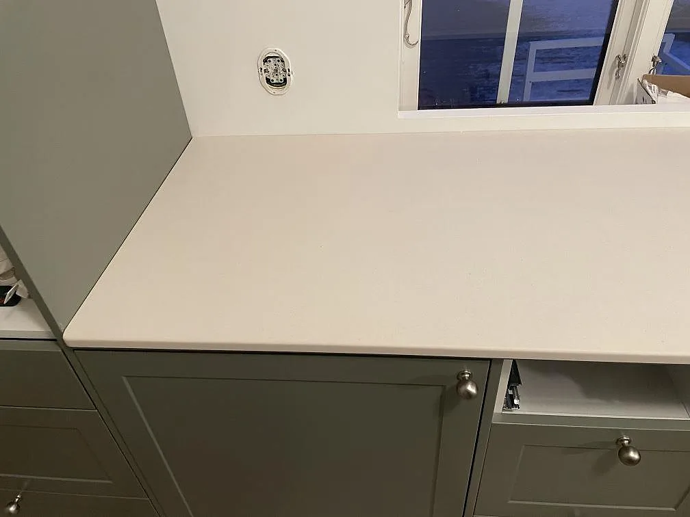 Närbild på matt gräddvit Dekton Aeris köksbänkskiva ovanpå gröngröna köksstommar i Tjörnarp.