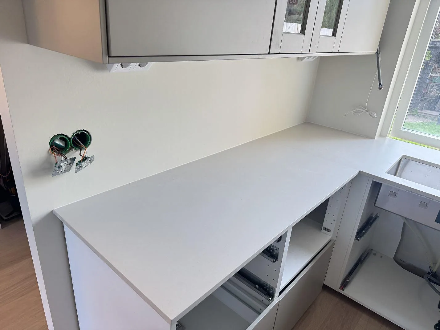 Lång arbetsyta i matt Dekton Aeris keramik under väggskåp, med öppna stommar och eluttag i Ystad.