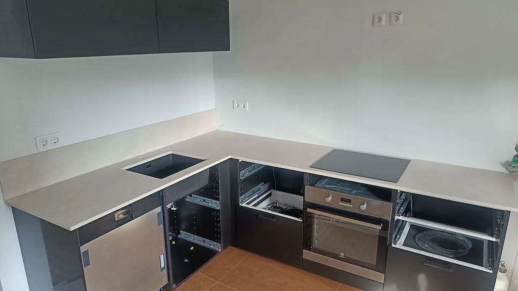 L-formad köksbänkskiva i matt Dekton Albarium keramik med svart underlimmad diskho och svart induktionshäll i ett kök i Bunkeflostrand.