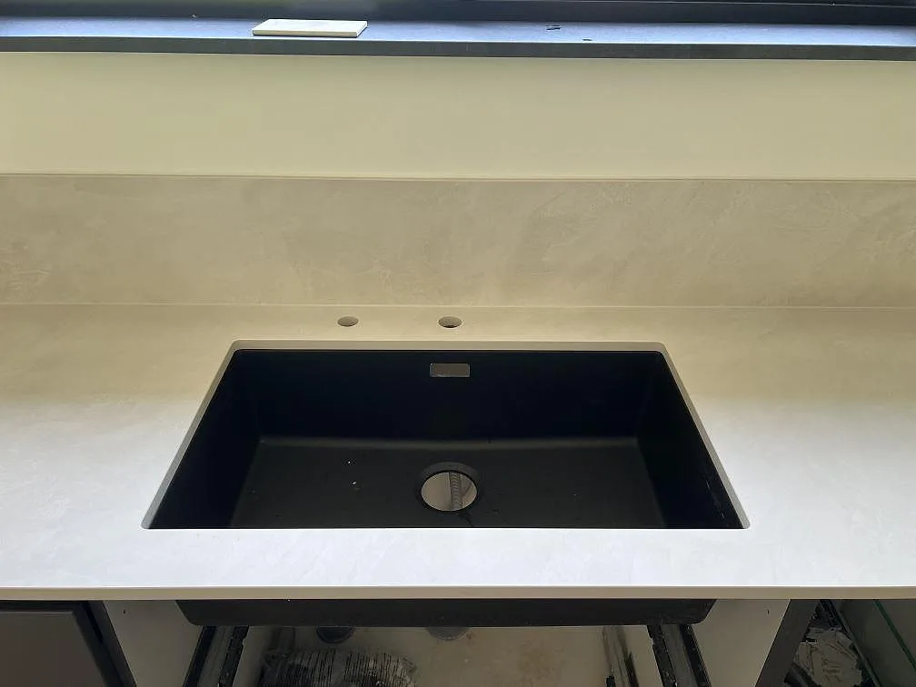 Detalj av matt Dekton Albarium runt en mörk diskho och smalt stänkskydd i ett kök i Höllviken.