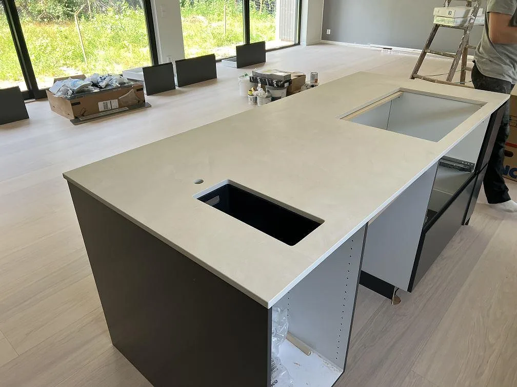 Köksö med matt Dekton Albarium i ljus keramik och synliga urtag i ett kök under montering i Höllviken.