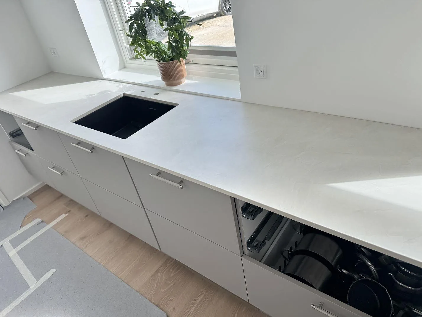 Matt Dekton Albarium som ljus köksbänkskiva med svart diskho, diskret ådring och fönsterljus i ett kök i Hørsholm.