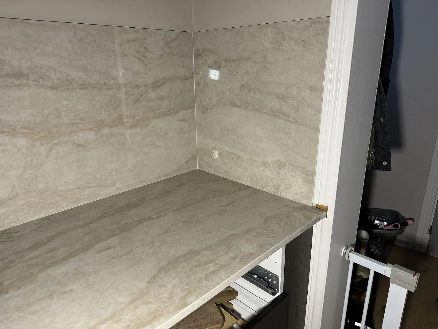 Hörn med köksbänkskiva och väggbeklädnad i polerad Dekton Arga över öppna vita stommar i Åryd.