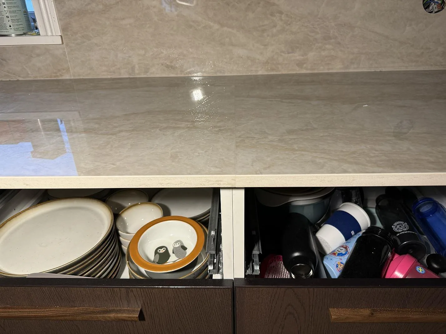 Rak frontvy av köksbänkskiva i polerad Dekton Arga över öppna lådor och mörka fronter i Åryd.