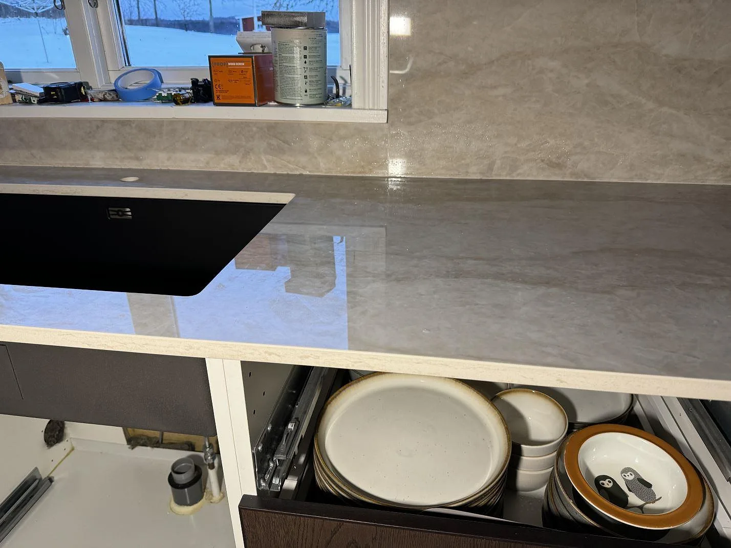 Köksbänkskiva i polerad Dekton Arga med svart underlimmad diskho och stänkskydd vid snöigt fönster i Åryd.