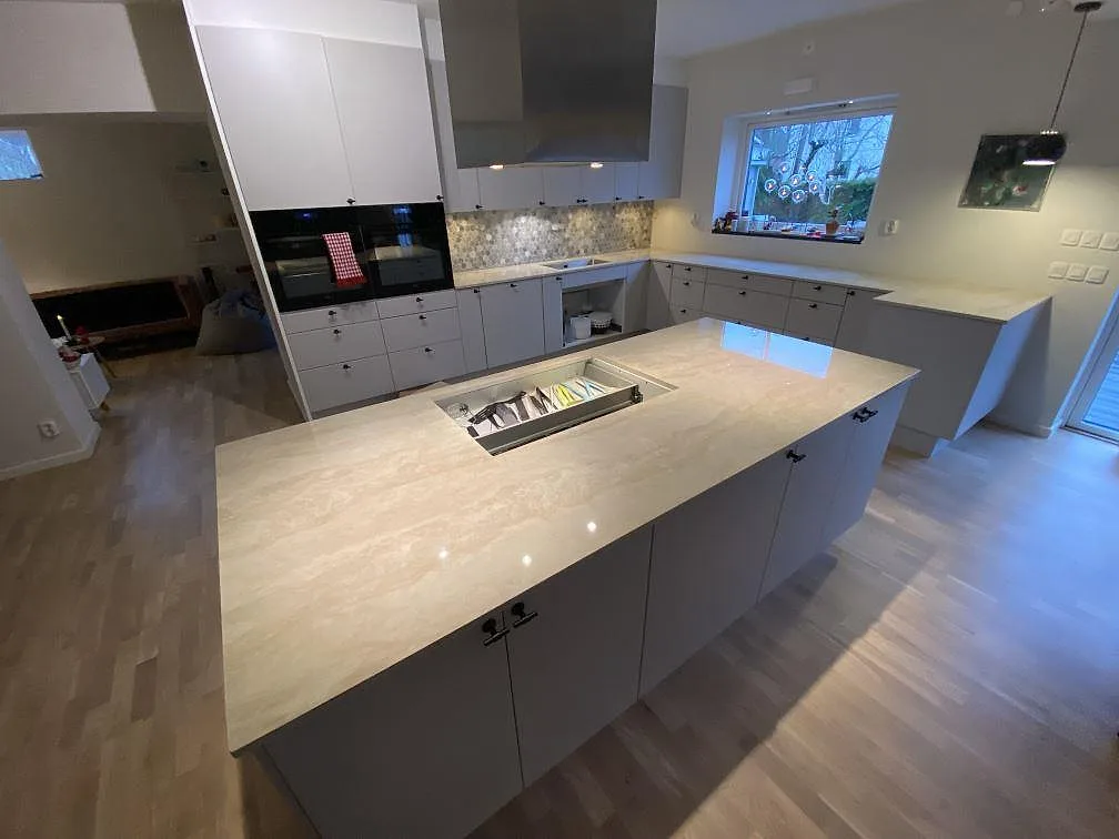 Köksbänkskiva i krämbeige Dekton Arga, polerad, med köksö och L-formad bänk i ett kök under montering i Älvsjö.