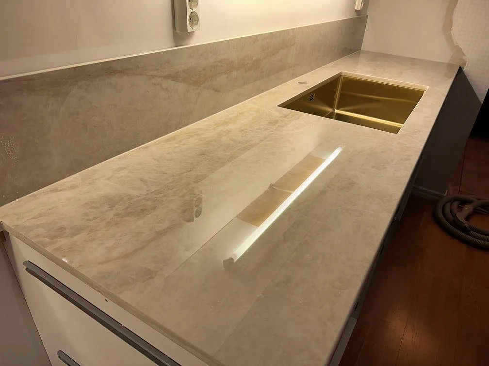 Köksbänk i Dekton Arga, polerad, med mässingstonad diskho och ljus stenådring i Ängelholm.