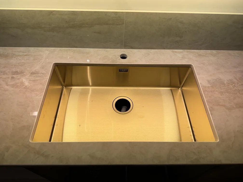 Närbild på mässingstonad underlimmad diskho i polerad Dekton Arga med stänkskydd i Ängelholm.