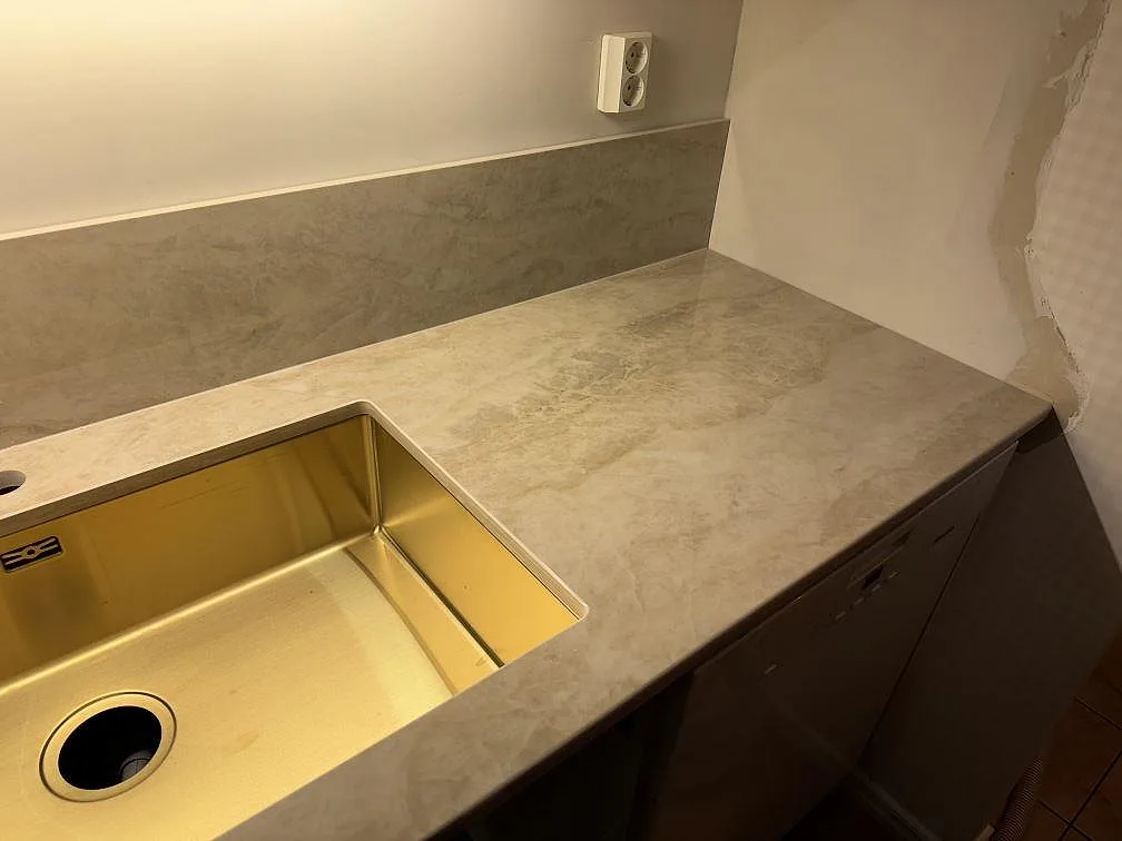 Diskbänksdel i polerad Dekton Arga med undermonterad mässingstonad diskho och varm ådring i Ängelholm.