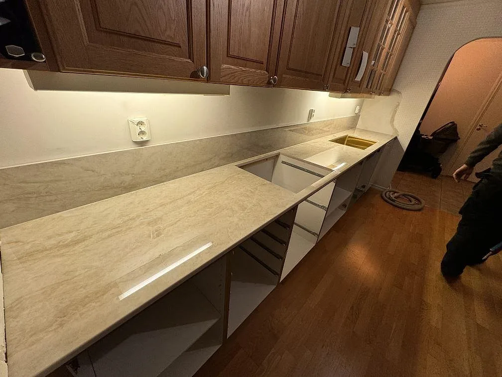 Köksbänkskiva i polerad Dekton Arga med stänkskydd, hälluttag och mässingstonad diskho i ett kök i Ängelholm.