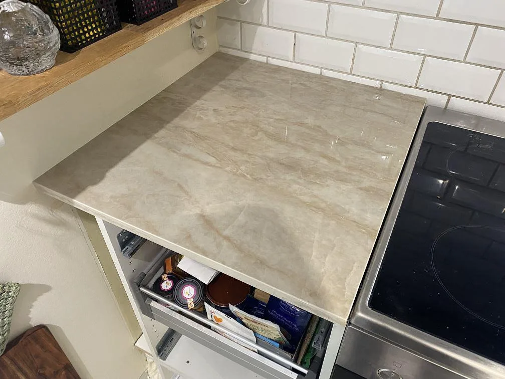 Detalj av polerad Dekton Arga keramik på köksbänk bredvid svart spis, med beige ådring i ett kök i Alingsås.