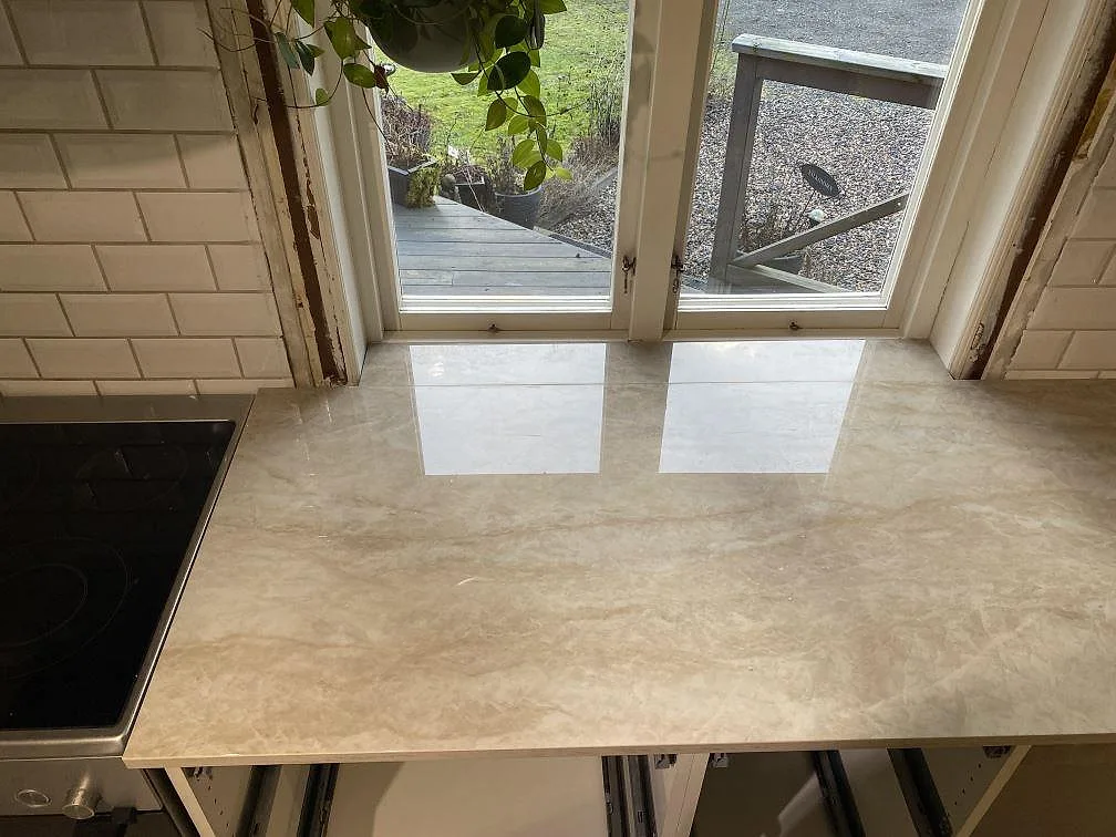 Polerad köksbänkskiva i Dekton Arga keramik under fönster, med ljus reflektion och mjuk ådring i Alingsås.