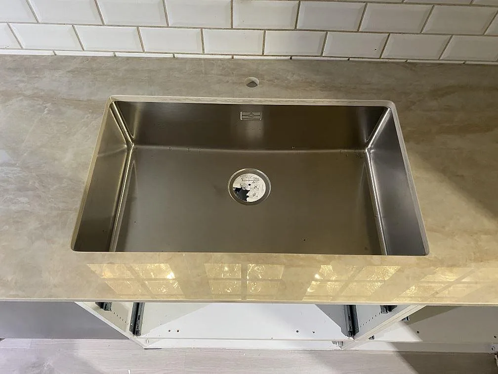 Närbild på diskho i polerad Dekton Arga keramik, med blank cremebeige bänkskiva mot vitt kakel i Alingsås.