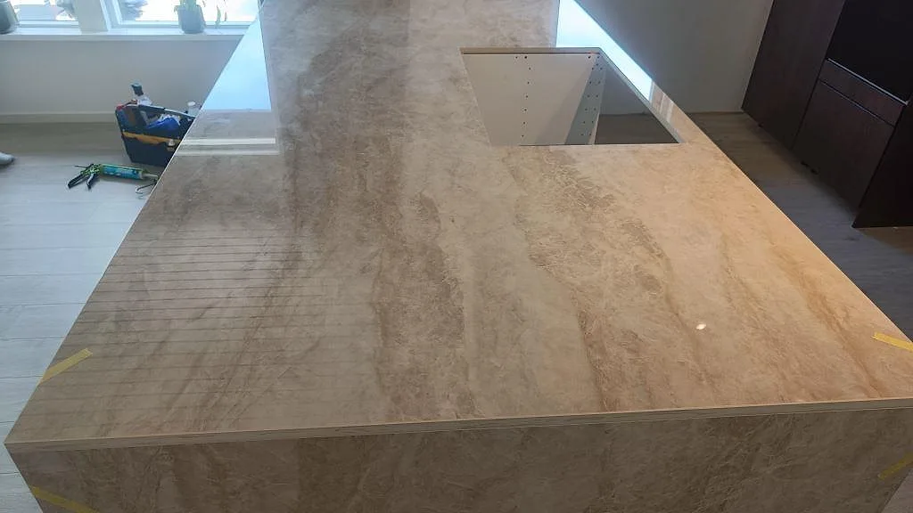 Närbild på den polerade Dekton Arga-ytan på köksön med rektangulärt urtag och speglingar från fönster i Alvesta.