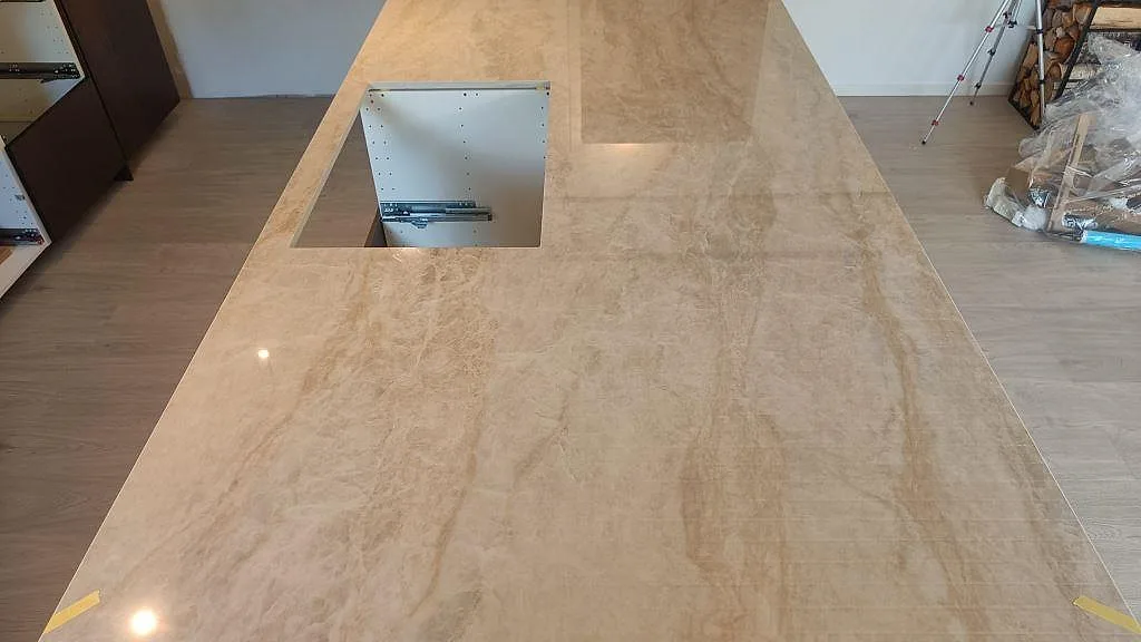Ovanvy av köksö i polerad Dekton Arga med rektangulärt urtag, beige ådring och ljus trägolvsmiljö i Alvesta.
