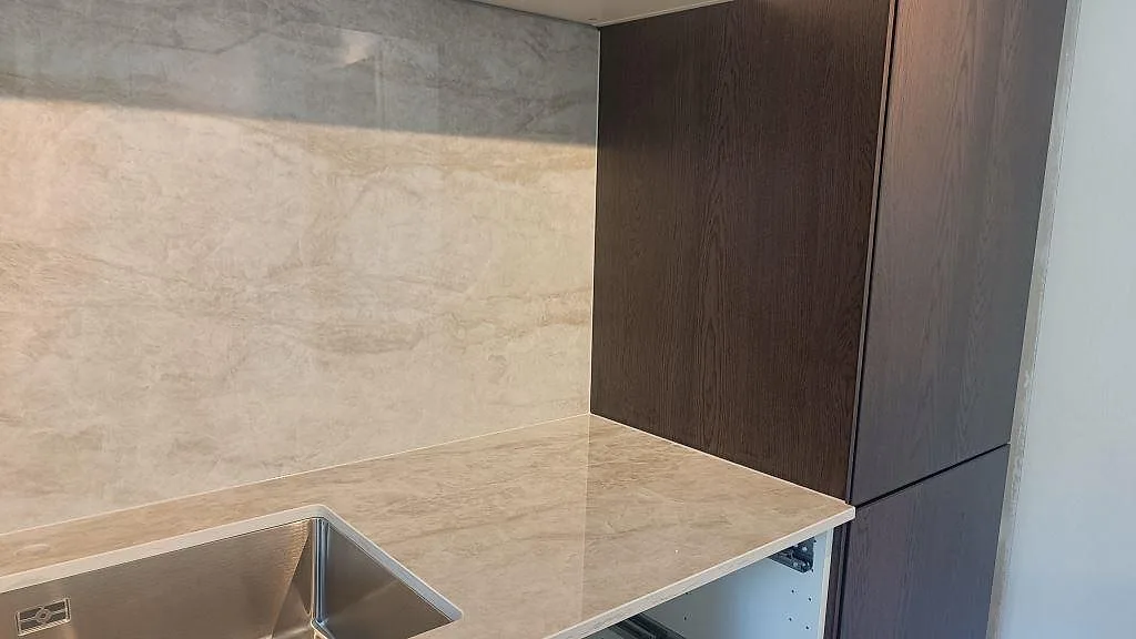 Bakre bänkrad i polerad Dekton Arga med rostfri underlimmad diskho och 8 mm väggpanel i ett kök i Alvesta.