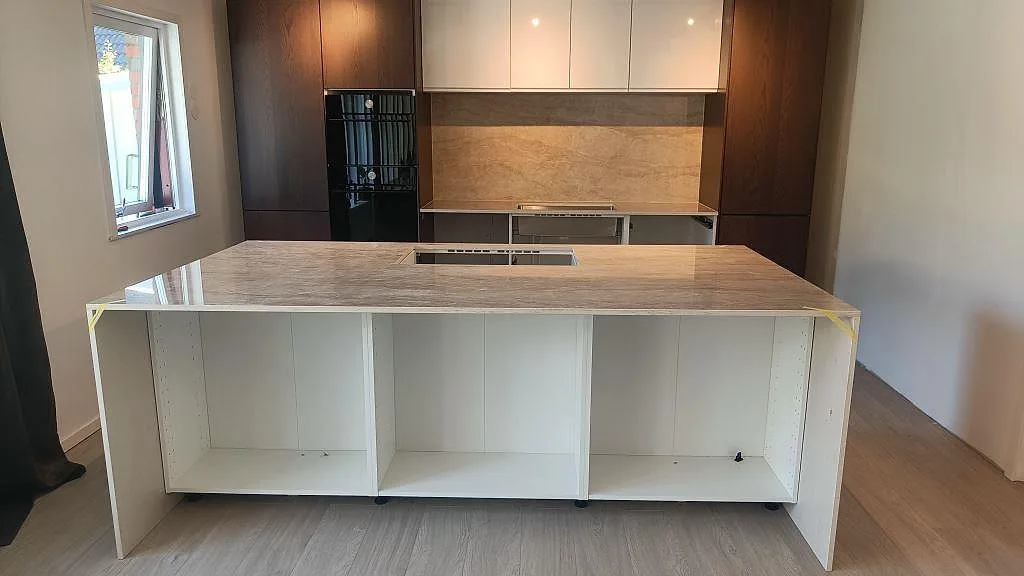 Köksbänkskiva i 20 mm polerad Dekton Arga med stor köksö, ljus väggbeklädnad och mörka träskåp i Alvesta.