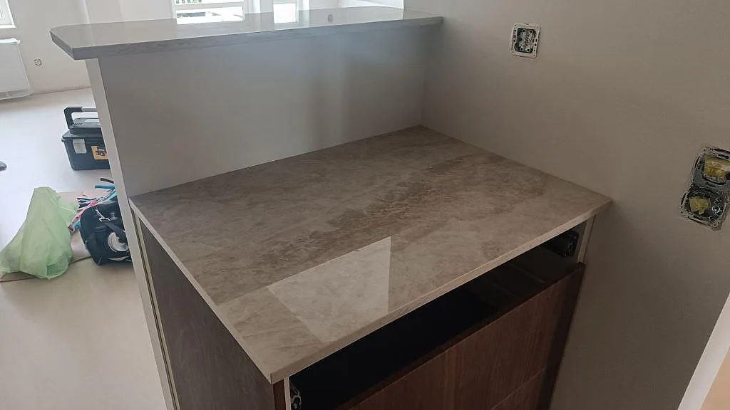 Köksbänkskiva i polerad Dekton Arga med beige travertinlik ådring på en peninsula i ett kök i Arlöv.