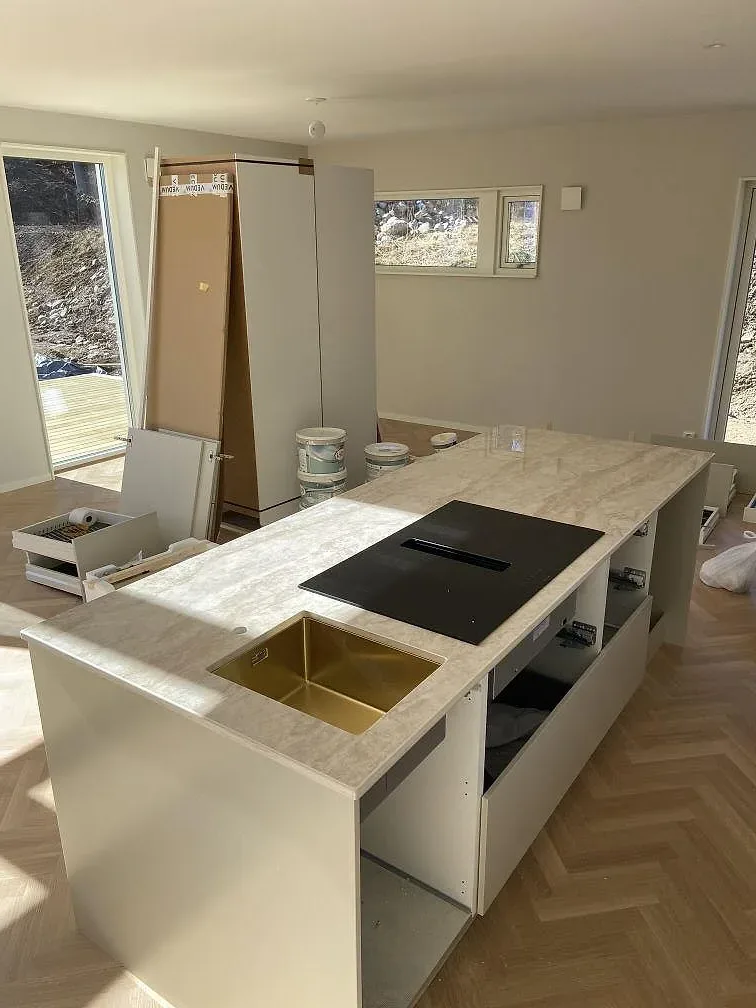 Köksö i vit Dekton Arga keramik med matt yta, svart induktionshäll och underlimmad diskho i mässingston, monterad i ett kök i Båstad.