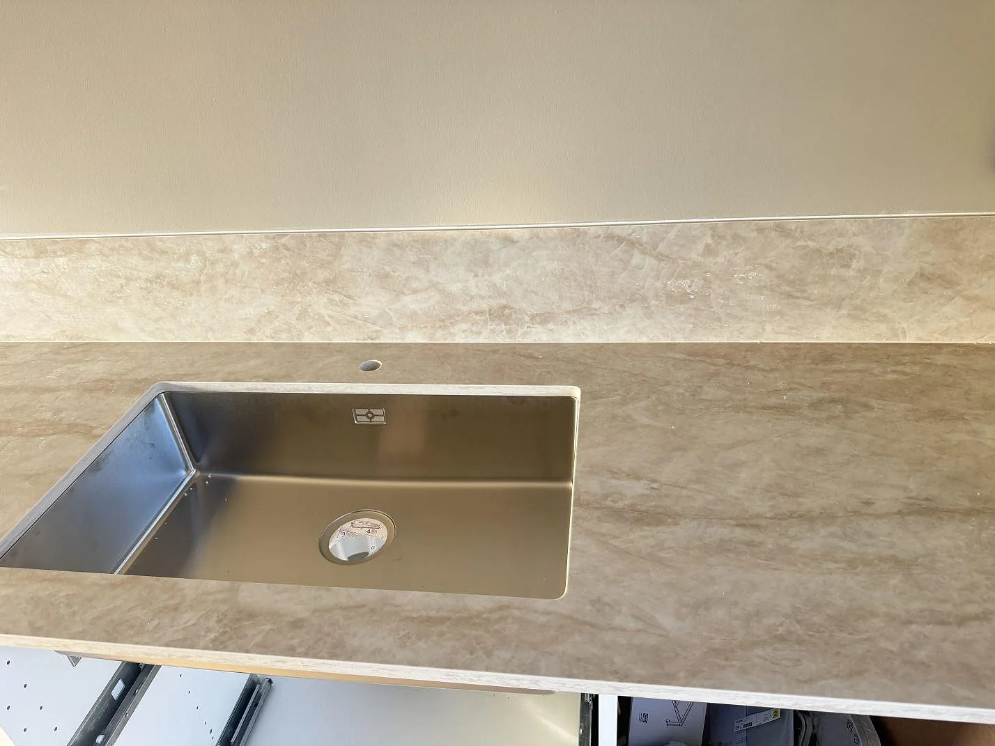 Detalj av polerad Dekton Arga bänkskiva i keramik med diskho och låg stänkkant längs väggen i Bankeryd.