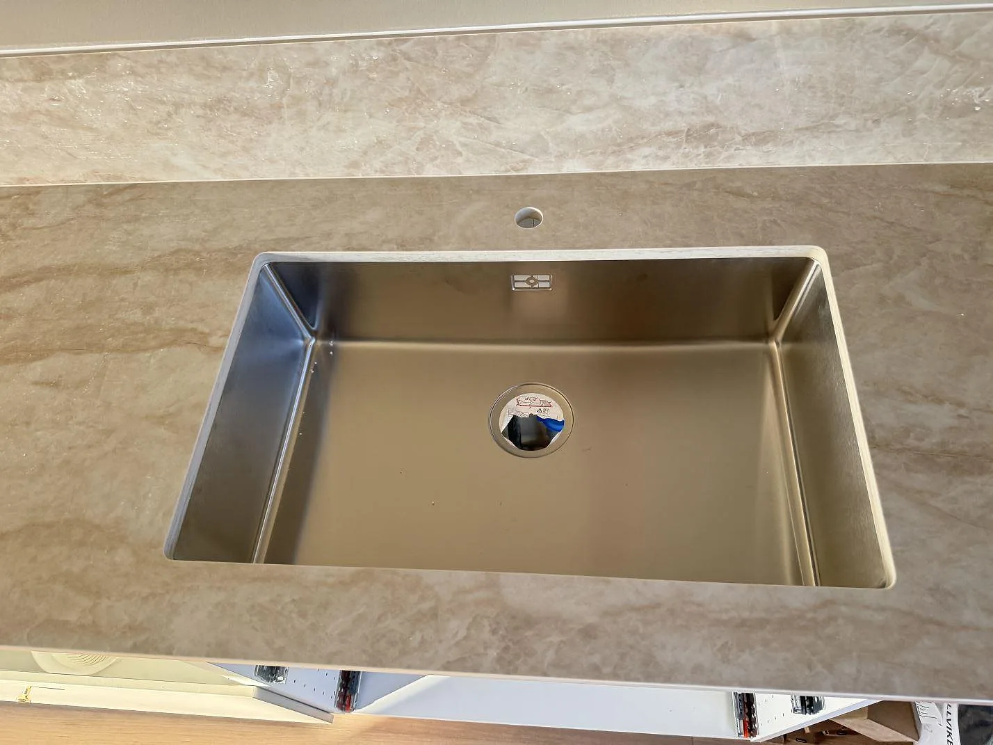 Närbild av diskho i polerad Dekton Arga köksbänkskiva med beigegrå ådring och stänkkant i Bankeryd.