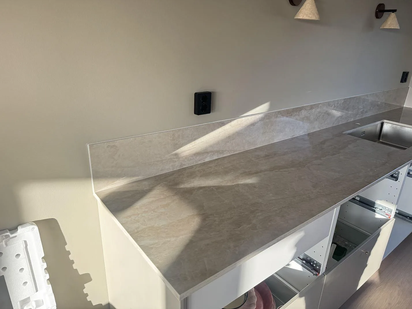 Väggbänk i polerad Dekton Arga keramik med låg stänkkant och synlig diskhozon under montering i Bankeryd.