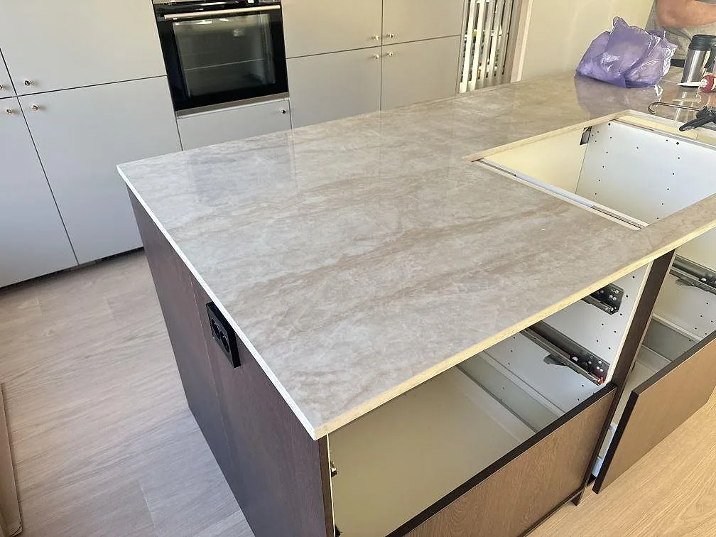 Polerad Dekton Arga bänkskiva i keramik på köksö med ljus beigegrå ådring och öppning i skivan i Bankeryd.