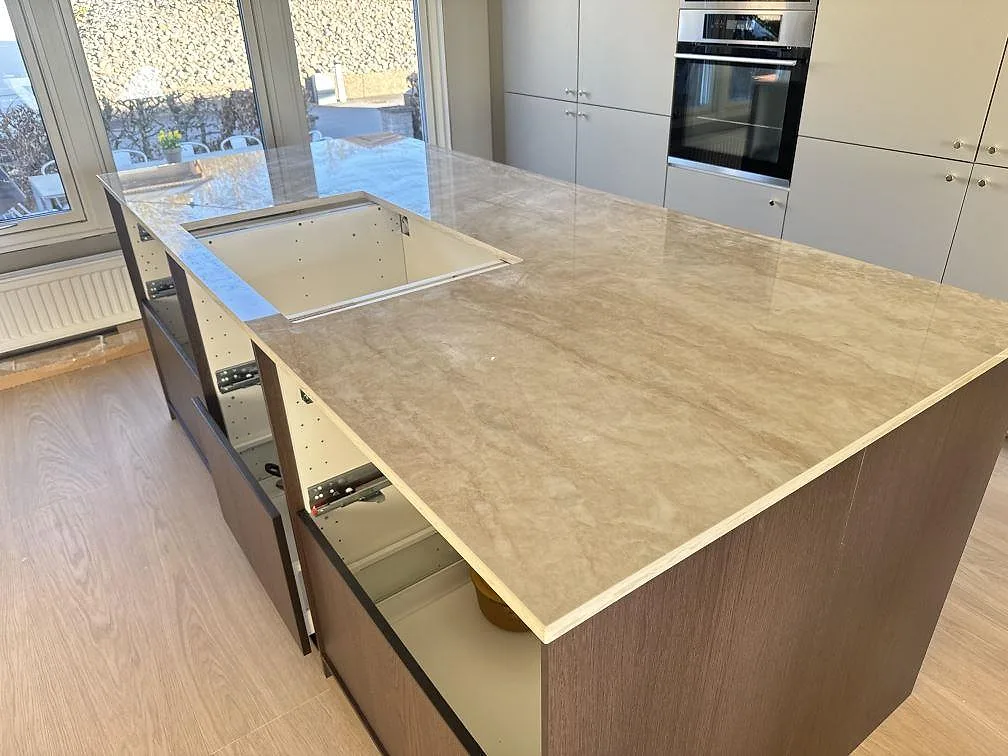 Köksö i 20 mm polerad Dekton Arga keramik med stor sammanhängande arbetsyta och öppna stommar under montering i Bankeryd.