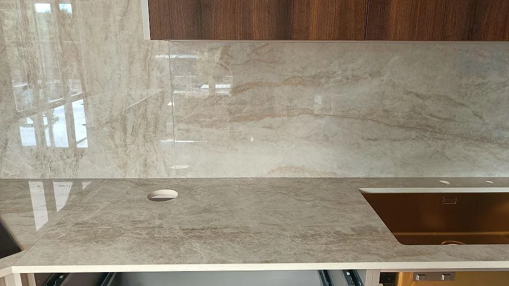 Köksbänkskiva i Dekton Arga, polerad ljusgrå sintersten med mjuk ådring, med heltäckande stänkvägg i samma sten i ett kök i Barsebäck.