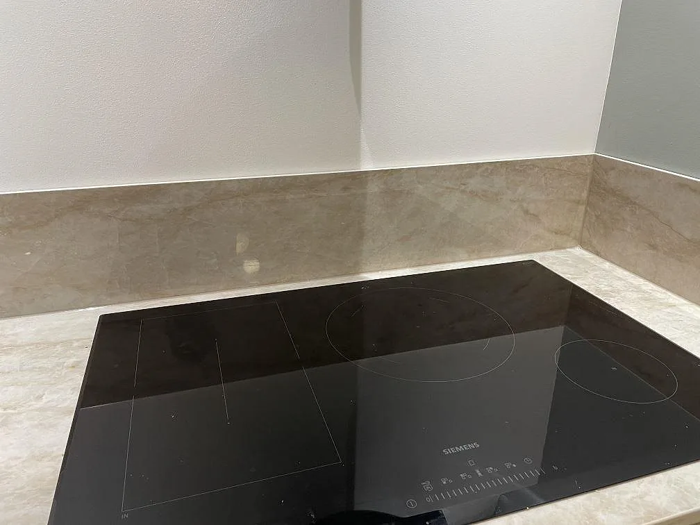 Infälld Siemens induktionshäll i en polerad Dekton Arga köksbänkskiva med uppvikt stänkkant i samma keramiksten i ett kök i Billdal.