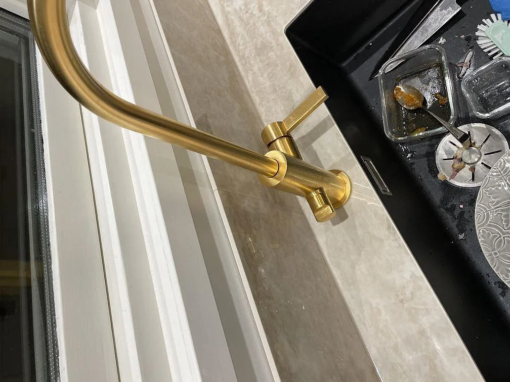 Närbild av mässingsblandare, svart diskho och polerad Dekton Arga bänkskiva vid fönster i Billdal.