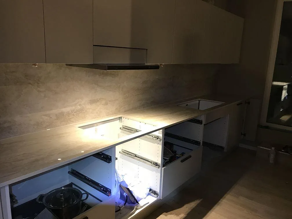 Köksbänkskiva och uppvikt stänkskydd i ljusgrå marmorlik Dekton Arga i ett L-format kök under montering