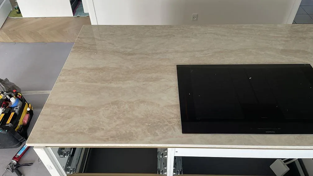 Köksö i polerad Dekton Arga med svart induktionshäll och ljus ådring i ett kök under montering i Brøndby Strand.
