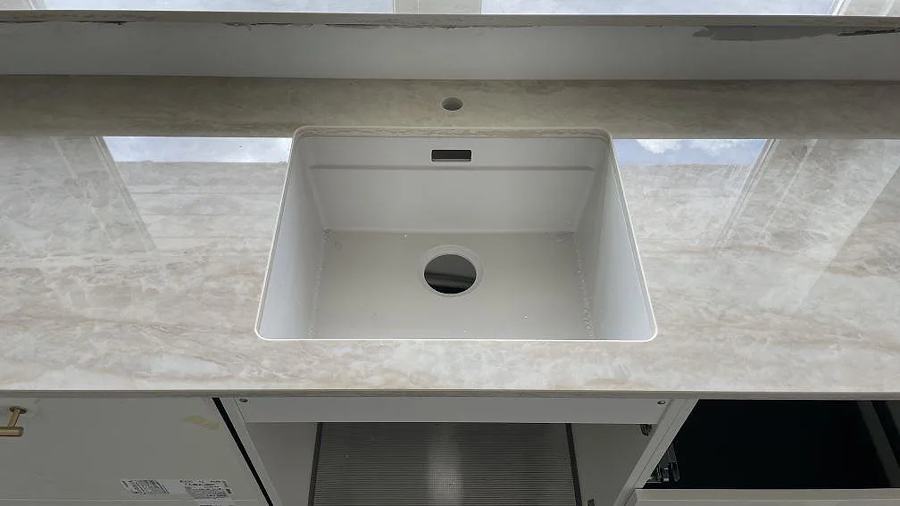 Närbild på vit underlimmad diskho i polerad Dekton Arga köksbänkskiva med blank reflektion från fönstret i Brøndby Strand.