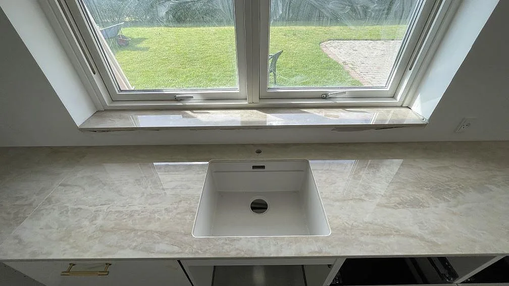 Köksbänk i polerad Dekton Arga med vit underlimmad diskho under ett fönster i Brøndby Strand.