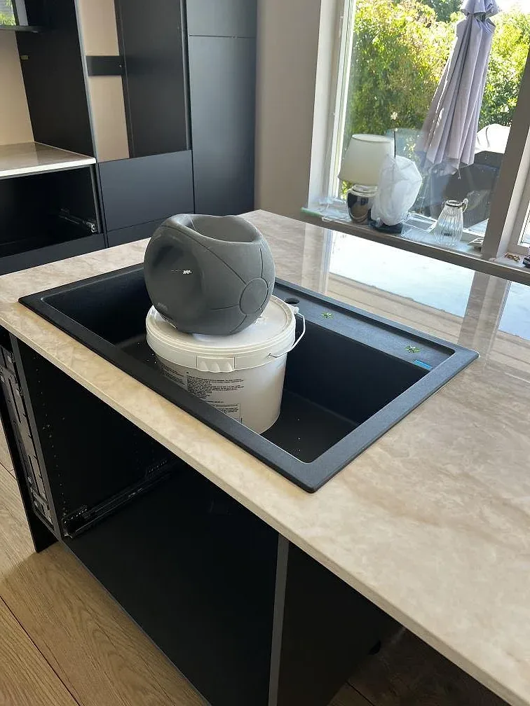 Rostfri underlimmad diskho i polerad Dekton Arga med svart köksinredning och stor fönsteröppning i Bromölla.