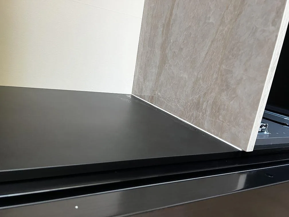 Detalj av polerad Dekton Arga där bänkskivan möter svart inredning och en lodrät stenklädd sida i köket i Bromölla.