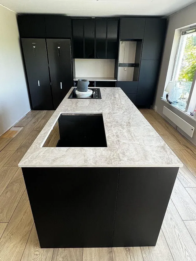 Köksö i polerad Dekton Arga keramik med hälluttag, rostfri underlimmad diskho och svarta köksstommar i ett kök i Bromölla.