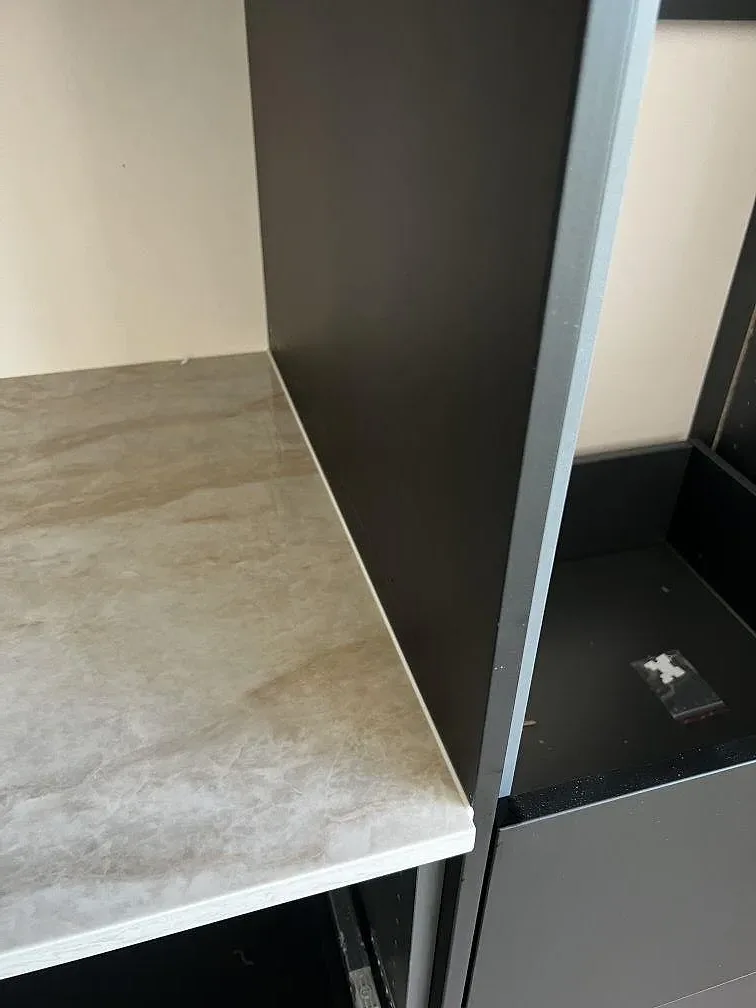 Kantdetalj i polerad Dekton Arga med ljus travertinlik ådring intill svarta köksstommar i Bromölla.