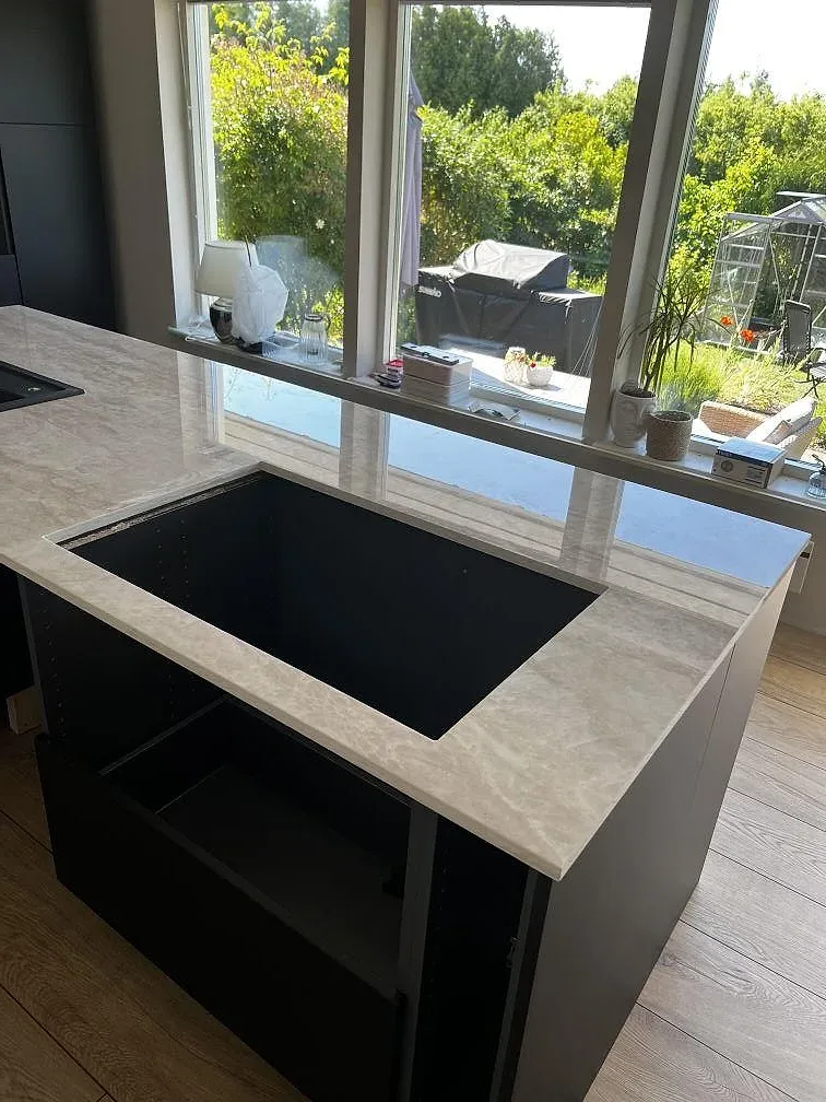 Närbild på hälluttaget i en köksö av polerad Dekton Arga med ljus ådring och fönsterljus i Bromölla.
