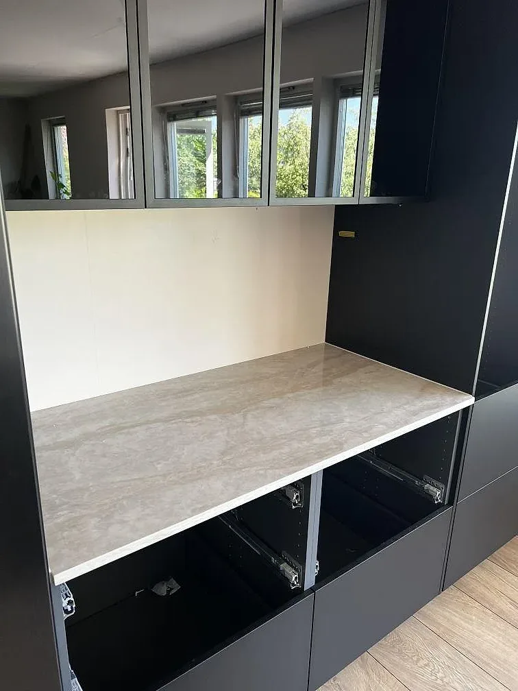 Rak bänkyta i polerad Dekton Arga monterad mellan svarta köksstommar och speglande skåpsluckor i Bromölla.