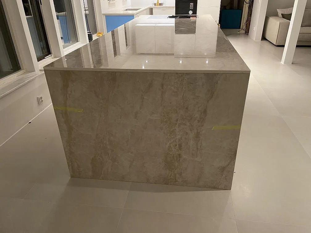 Köksö i polerad Dekton Arga med gråbeige ådring och ljusa skåp i ett kök i Bunkeflostrand.