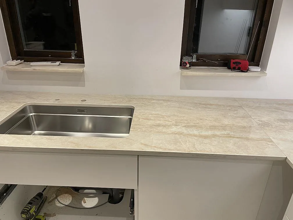 Köksbänkskiva i Dekton Arga, polerad krämvit keramik, med underlimmad rostfri diskho framför två fönster i ett kök i Bunkeflostrand.