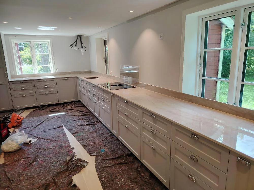 Köksbänkskiva i polerad Dekton Arga keramik med ljus ådring och stänkkant i ett U-format kök i Enköping.