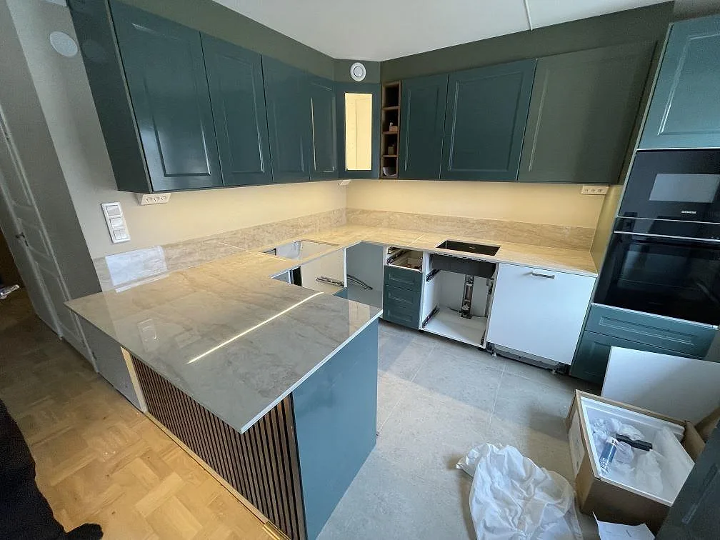 Polerad keramikbänkskiva i Dekton Arga med halvö, stänkskydd och synlig häll i ett U-format kök i Enskededalen.
